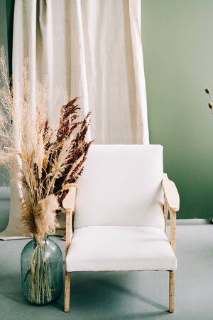a stylish white chair stands in a spacious Studio , next to a glass vase with dry branches of flowers ,の写真素材