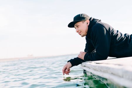 a young guy in sports black clothes sits on a pier near the lakeの写真素材