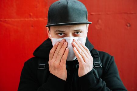 a young man in black sportswear and a baseball cap with a medical mask on his face near the red...