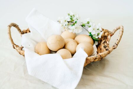 on the table is a natural wicker basket with several Easter eggs with cracks on a white napkin,...
