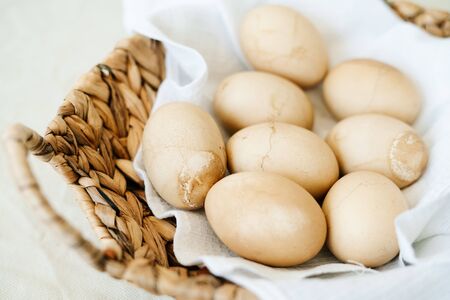 in a natural wicker basket made of seaweed, eight Easter eggs with cracks on a white napkin, painted...