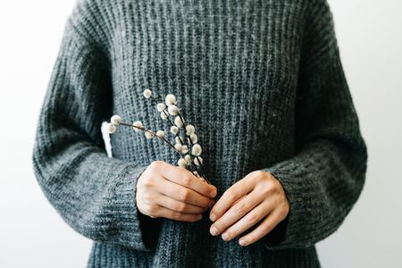 a smiling Girl in a gray knitted sweater holds natural branches of a budding willow in her hands.Minimal style.の写真素材