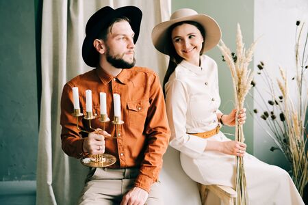 a couple in love in trendy clothes and hats are sitting on a brown sofa, embracing in a spacious...