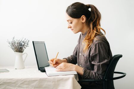 a young woman who works from home while the virus is quarantined on her laptop, studies information on the Internet and writes notes in a diary.A cosy working place,the concept of remote workの写真素材