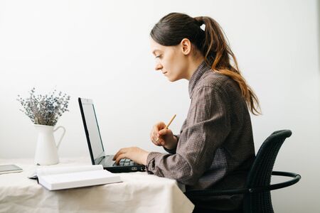 a young woman who works from home while the virus is quarantined on her laptop, studies information on the Internet and writes notes in a diary.A cosy working place,the concept of remote workの写真素材