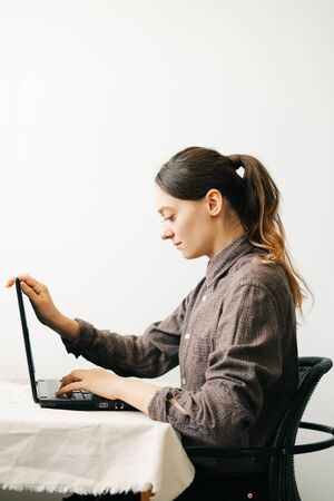 a young European woman, working from home during the virus quarantine, on her laptop. The girl is sitting at a white table, in a minimalistic interior.A cosy working place,the concept of remote work,の写真素材