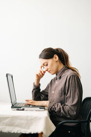 a young European woman, working from home during the virus quarantine, on her laptop. The girl is sitting at a white table, in a minimalistic interior.A cosy working place,the concept of remote work,の写真素材