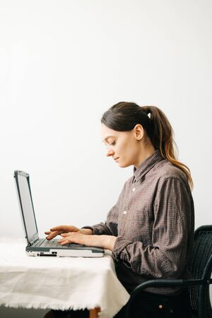 a young European woman, working from home during the virus quarantine, on her laptop. The girl is sitting at a white table, in a minimalistic interior.A cosy working place,the concept of remote work,の写真素材