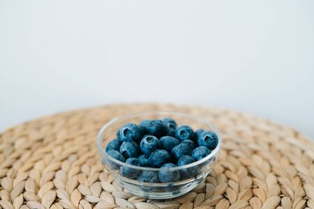 fresh ripe blueberries in a glass bowl on a natural wicker napkin made of dry seaweed on a white background. the concept of healthy foodの写真素材