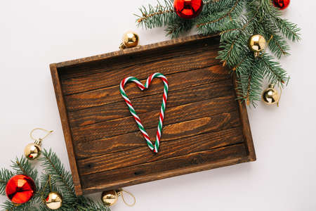 Christmas frame. Christmas balloons, garlands, red and gold ornaments, Christmas candles and fir branches with a brown wooden tray on a white background. Flatlay top view, copy spaceの写真素材