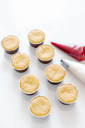 freshly baked cupcakes on a white table, next to the cooking sleeves with red strawberry berry filling and white cream cheese.Food for breakfast. Freshly baked cupcakes for dessert.の写真素材