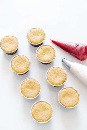 freshly baked cupcakes on a white table, next to the cooking sleeves with red strawberry berry filling and white cream cheese.Food for breakfast. Freshly baked cupcakes for dessert.の写真素材