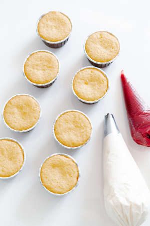 freshly baked cupcakes on a white table, next to the cooking sleeves with red strawberry berry filling and white cream cheese.Food for breakfast. Freshly baked cupcakes for dessert.の写真素材