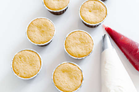 freshly baked cupcakes on a white table, next to the cooking sleeves with red strawberry berry filling and white cream cheese.Food for breakfast. Freshly baked cupcakes for dessert.の写真素材