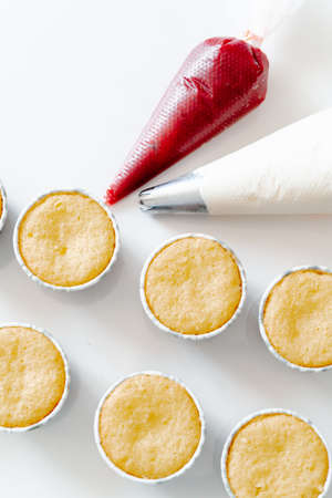freshly baked cupcakes on a white table, next to the cooking sleeves with red strawberry berry filling and white cream cheese.Food for breakfast. Freshly baked cupcakes for dessert.の写真素材