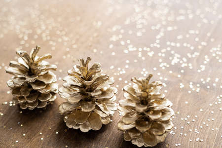 natural golden cones on a wooden table with gold spangles in the shape of stars, among fir branchesの写真素材