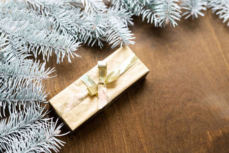 a golden gift box on a wooden table among fir branches with warm light bulbsの写真素材
