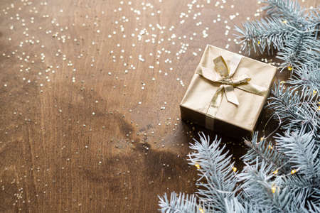 a golden gift box on a wooden table among fir branches with warm light bulbsの写真素材