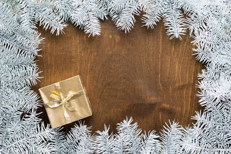 a golden gift box on a wooden table among fir branches with warm light bulbsの写真素材