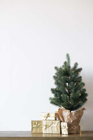 a small Christmas tree with warm bulbs in a pot on a wooden table with gifts wrapped in gold paper. the concept of Christmas. High quality photoの写真素材