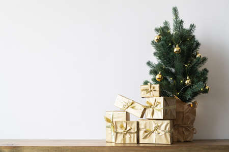 a small Christmas tree with warm bulbs in a pot on a wooden table with gifts wrapped in gold paper. the concept of Christmas. High quality photoの写真素材