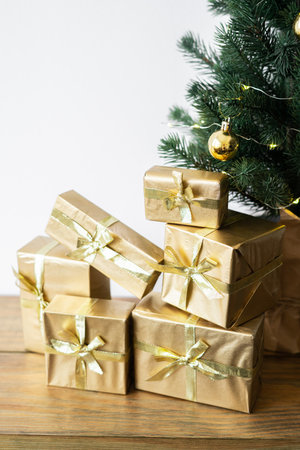 a small Christmas tree with warm bulbs in a pot on a wooden table with gifts wrapped in gold paper. the concept of Christmas. High quality photoの写真素材