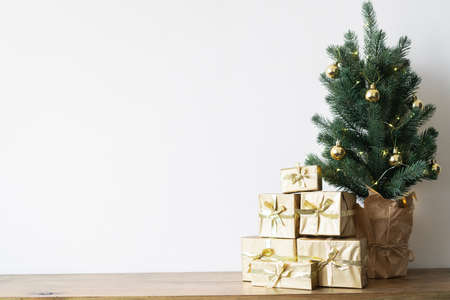 a small Christmas tree with warm bulbs in a pot on a wooden table with gifts wrapped in gold paper. the concept of Christmasの写真素材