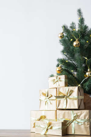 a small Christmas tree with warm bulbs in a pot on a wooden table with gifts wrapped in gold paper. the concept of Christmasの写真素材