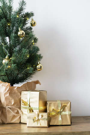 a small Christmas tree with warm bulbs in a pot on a wooden table with gifts wrapped in gold paper. the concept of Christmas. High quality photoの写真素材