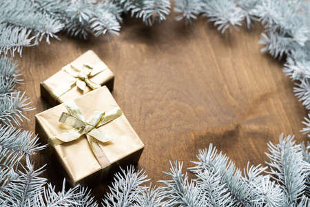 a golden gift box on a wooden table among fir branches with warm light bulbs. High quality photoの写真素材