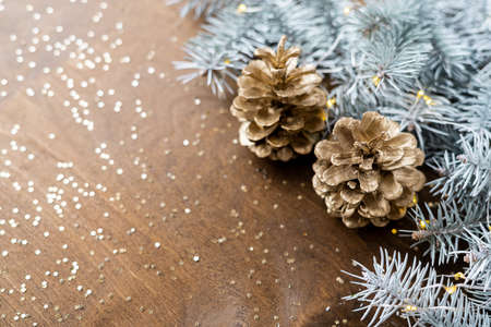 natural golden cones on a wooden table with gold spangles in the shape of stars, among fir branches with warm light bulbs.の写真素材