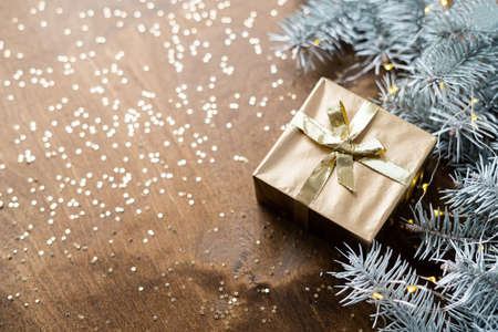 a golden gift box on a wooden table among fir branches with warm light bulbs. High quality photoの写真素材