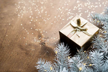 a golden gift box on a wooden table among fir branches with warm light bulbs. High quality photoの写真素材