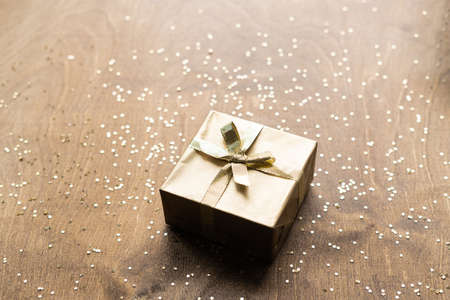 a golden gift box on a wooden table strewn with gold spangles in the shape of stars. the concept of Christmas. High quality photoの写真素材