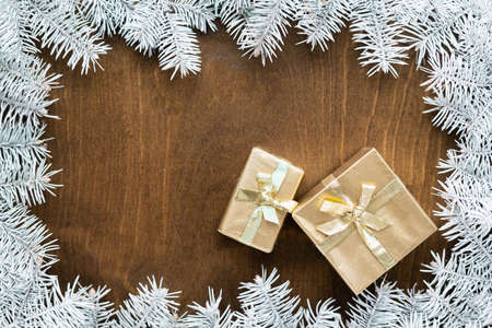 a golden gift box on a wooden table among fir branches with warm light bulbs. High quality photoの写真素材