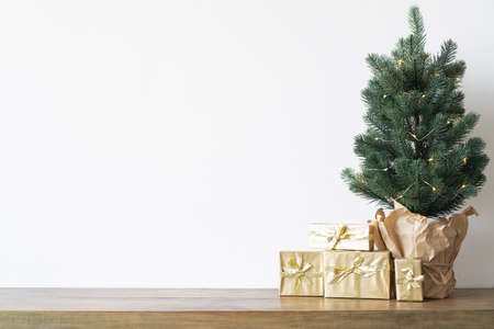 a small Christmas tree with warm bulbs in a pot on a wooden table with gifts wrapped in gold paper. the concept of Christmas. High quality photoの写真素材