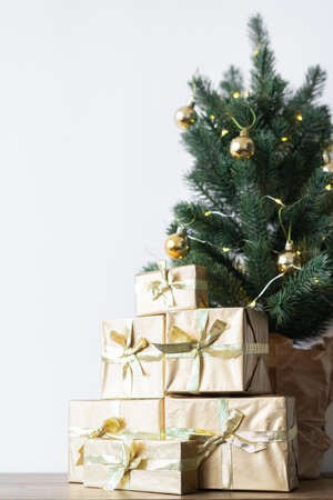 a small Christmas tree with warm bulbs in a pot on a wooden table with gifts wrapped in gold paper. the concept of Christmasの写真素材