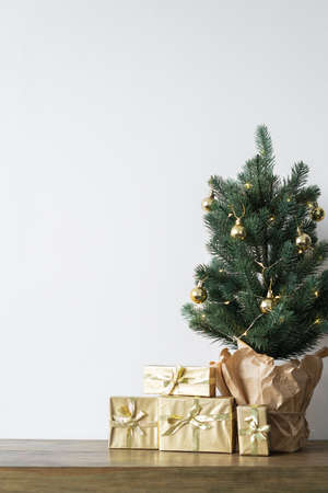 a small Christmas tree with warm bulbs in a pot on a wooden table with gifts wrapped in gold paper. the concept of Christmas. High quality photoの写真素材