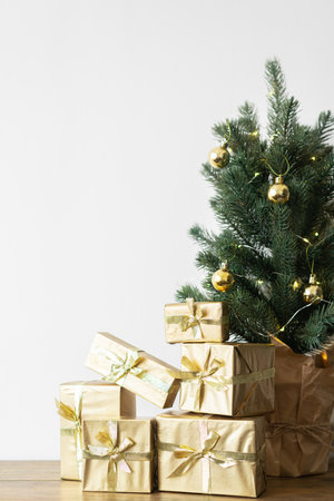 a small Christmas tree with warm bulbs in a pot on a wooden table with gifts wrapped in gold paper. the concept of Christmas. High quality photoの写真素材