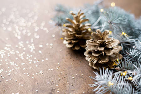 natural golden cones on a wooden table with gold spangles in the shape of stars, among fir branches with warm light bulbs.の写真素材