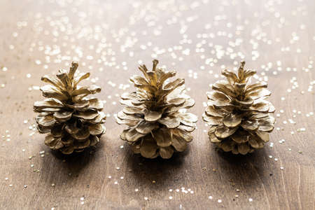 natural golden cones on a wooden table with gold spangles in the shape of stars, among fir branches.の写真素材