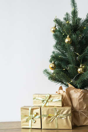 a small Christmas tree with warm bulbs in a pot on a wooden table with gifts wrapped in gold paper. the concept of Christmas. High quality photoの写真素材
