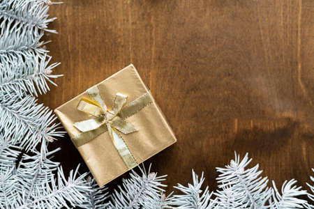 a golden gift box on a wooden table among fir branches with warm light bulbs. High quality photoの写真素材