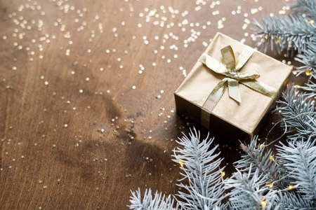 a golden gift box on a wooden table among fir branches with warm light bulbs. High quality photoの写真素材