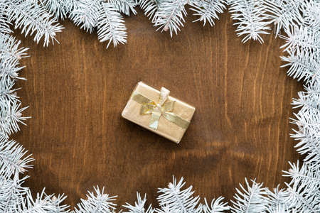 a golden gift box on a wooden table among fir branches with warm light bulbs. High quality photoの写真素材