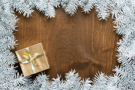 a golden gift box on a wooden table among fir branches with warm light bulbs. High quality photoの写真素材