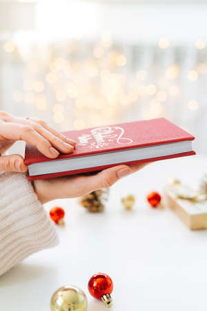 a red book in the hands of a young girl against the background of gifts and Christmas toys, a garland bokeh. the concept of Christmas. High quality photoの写真素材