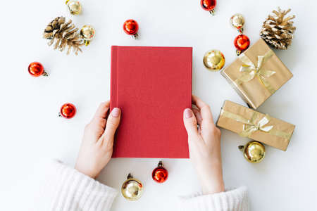 a red book in the hands of a young girl against the background of gifts and Christmas toys. the concept of Christmas. High quality photoの写真素材