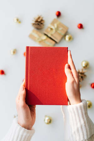 a red book in the hands of a young girl against the background of gifts and Christmas toys. the concept of Christmas. High quality photoの写真素材