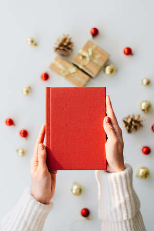 a red book in the hands of a young girl against the background of gifts and Christmas toys. the concept of Christmas. High quality photoの写真素材